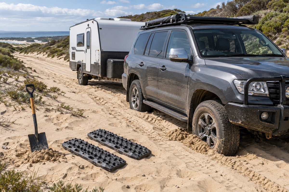 Four-wheel drive and caravan stopped in soft sand with shovel and traction boards nearby