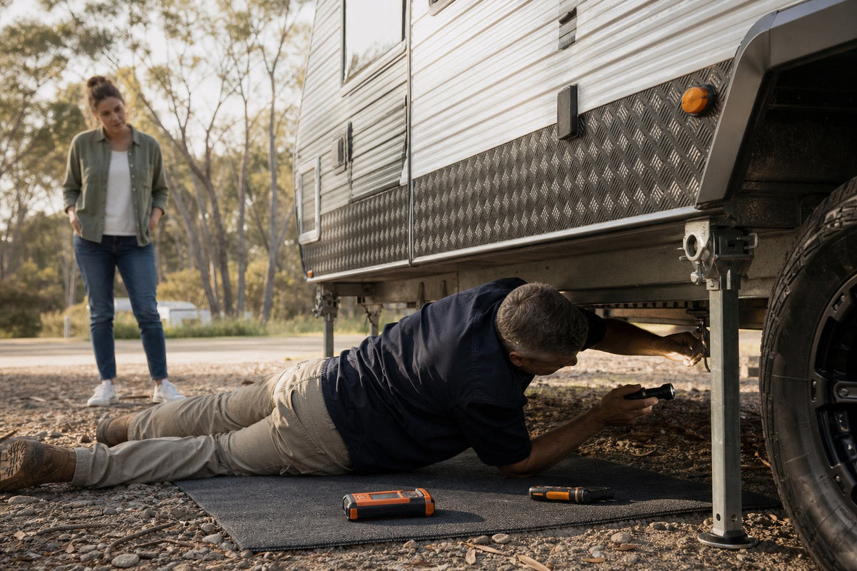 Independent caravan inspector using a torch to check beneath a used caravan while the buyer observes